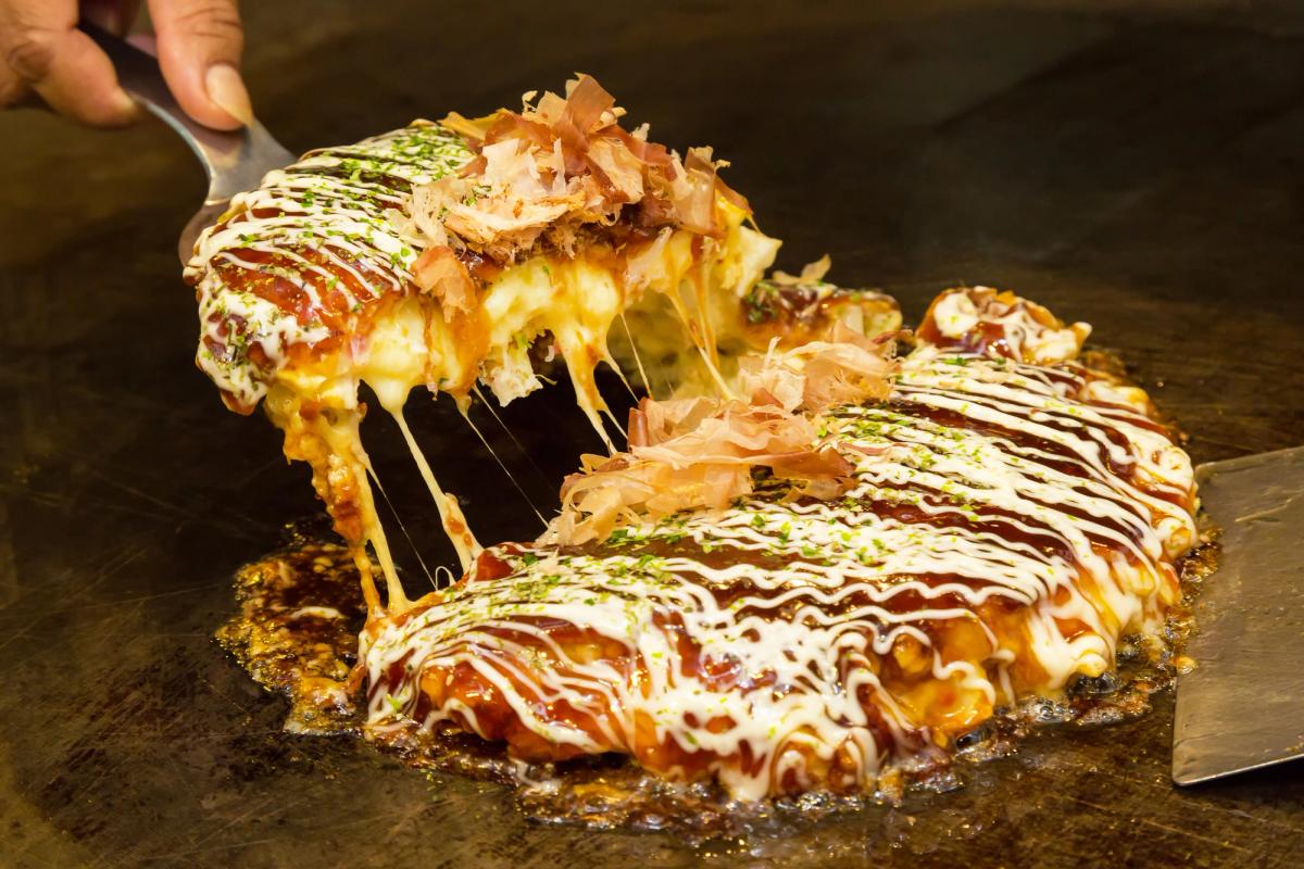 Okonomiyaki with melted cheese and bonito flakes, topped with takoyaki sauce drizzle