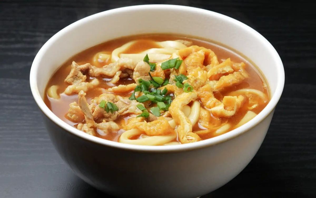 Bowl of udon noodles in spicy broth with meat and green onion garnish