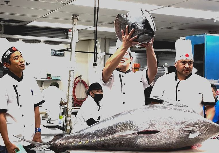 Chefs displaying large fresh tuna fish in professional kitchen setting