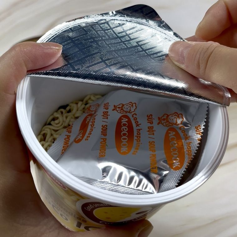 Instant ramen noodle cup with seasoning packet being opened by hand
