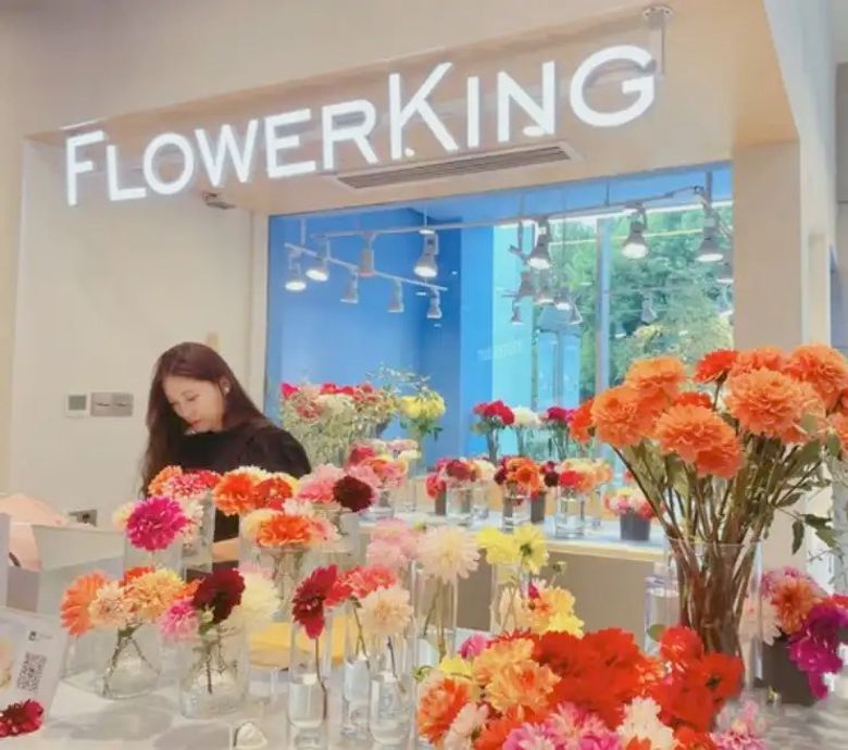 Flowerking florist shop interior with colorful gerbera daisies in glass vases and staff member