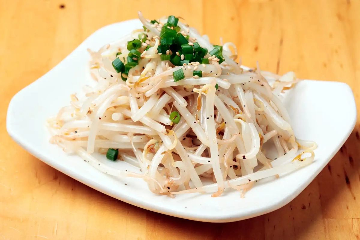 Bean sprouts with green onions and sesame seeds on white plate