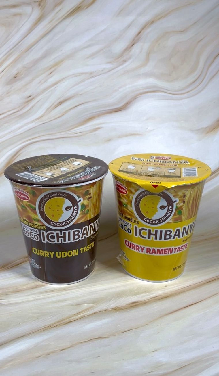 Two Coco Ichibanya instant ramen cups: Curry Udon and Curry Ramen flavors on marble surface