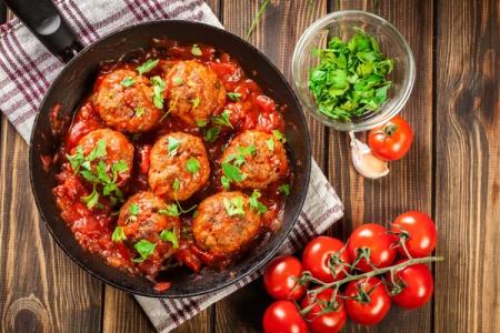 Meatballs in tomato sauce with fresh parsley garnish and ingredients on wooden table