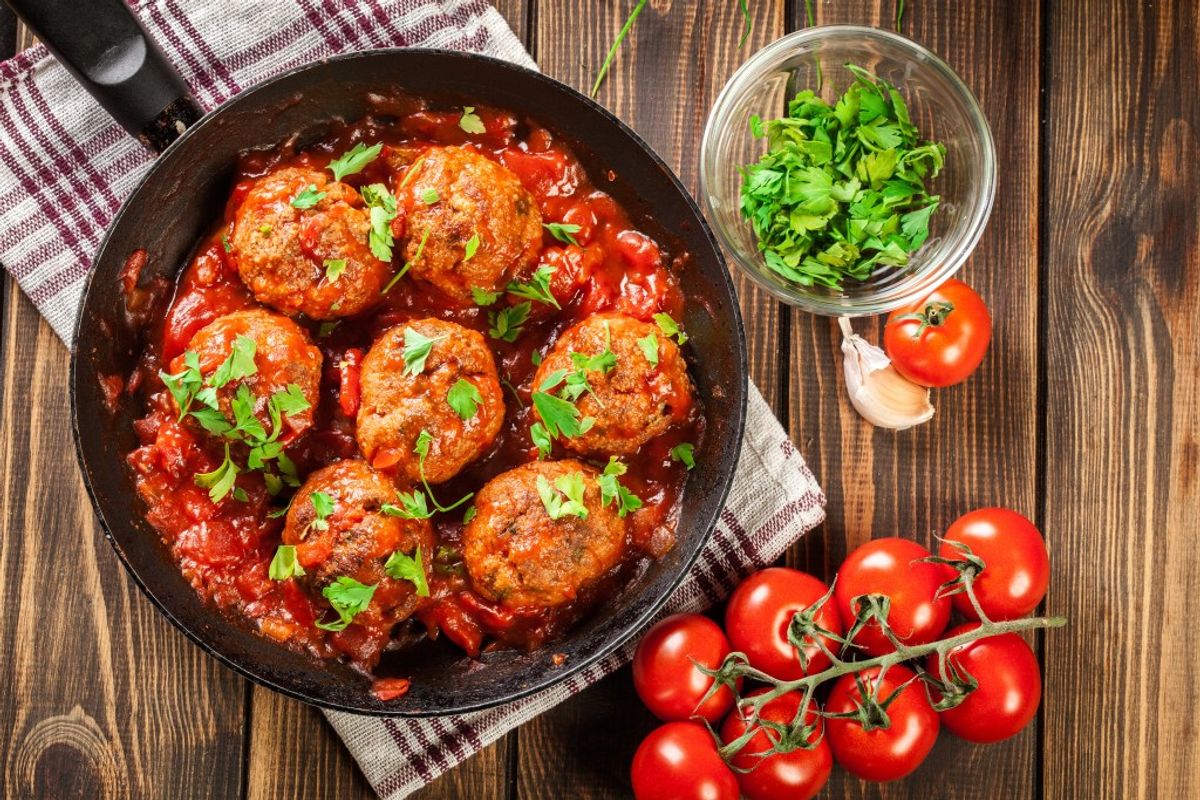 Meatballs in tomato sauce with fresh parsley, tomatoes, and garlic on wooden table