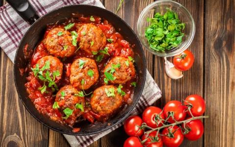 Meatballs in tomato sauce with fresh parsley garnish and ingredients on wooden table