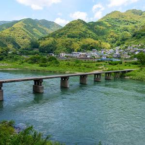 Japanese riverside village with traditional houses, green mountains, and concrete bridge crossing turquoise water