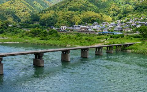Japanese riverside village with traditional houses, green mountains, and concrete bridge crossing turquoise water