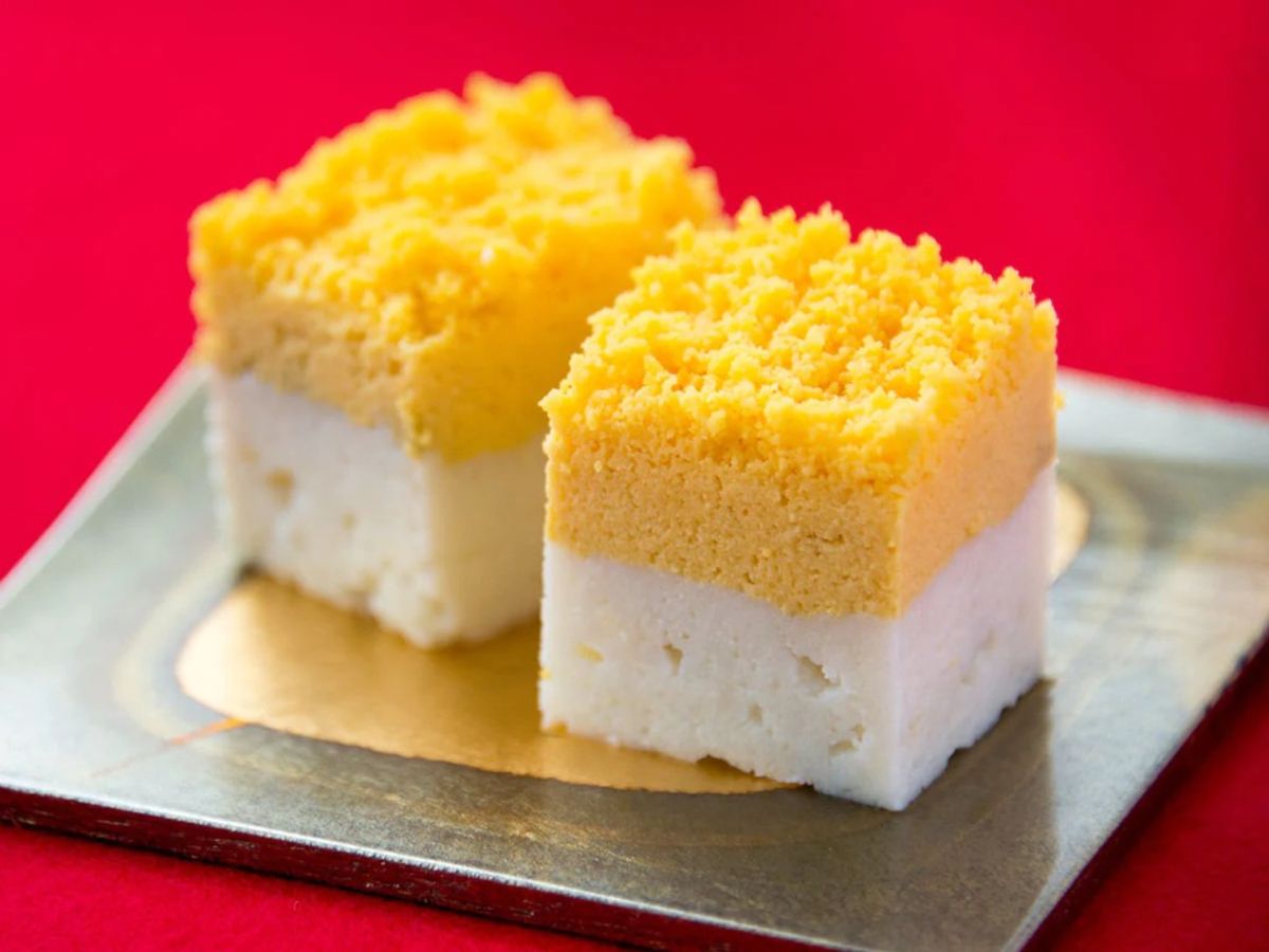 Two-layer sponge cake slices with yellow top and white cream filling on white plate, red background