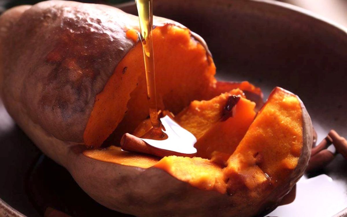 Baked sweet potato with butter being drizzled on top in a bowl