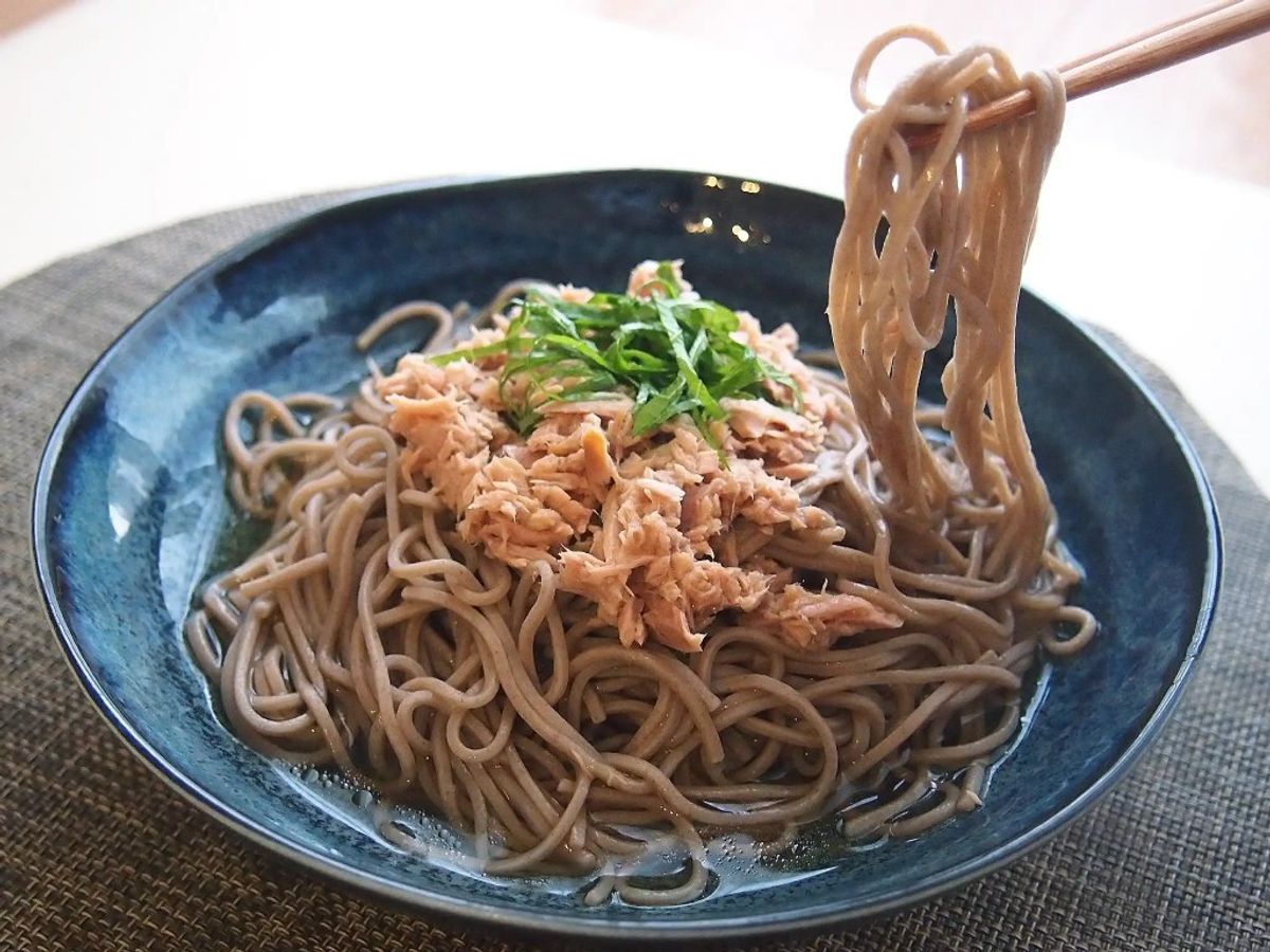 Buckwheat noodles with shredded chicken and green onions in blue bowl with chopsticks