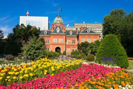 Red brick historic building with colorful flower garden under blue sky