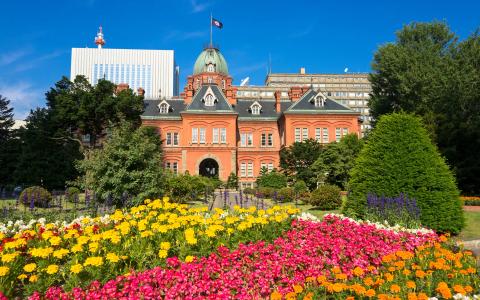 Red brick historic building with colorful flower garden under blue sky