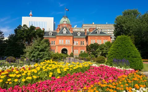 Red brick historic building with colorful flower garden under blue sky