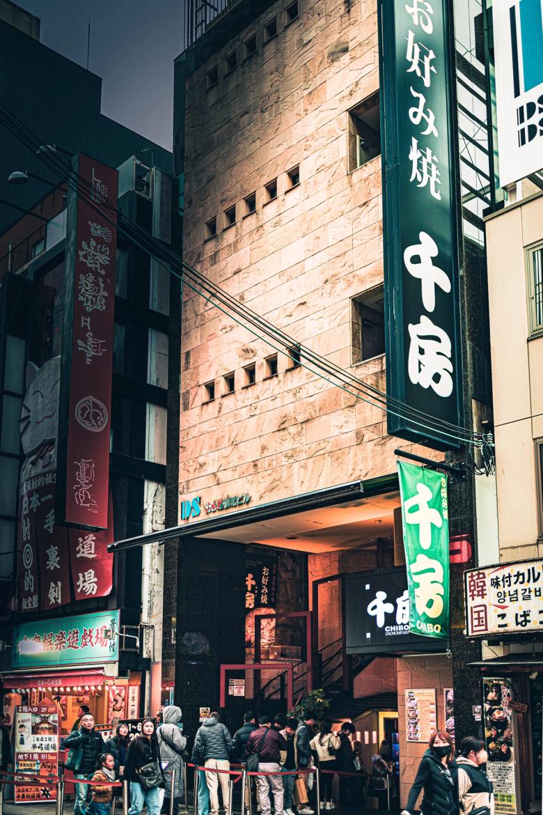 Busy Japanese yakitori restaurant storefront with green signage and queue of customers at night