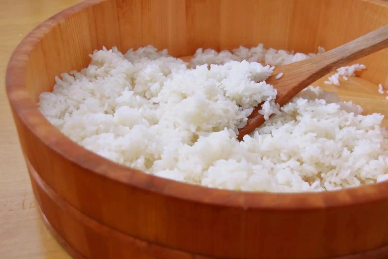 Freshly cooked white rice in wooden serving bowl with wooden spoon