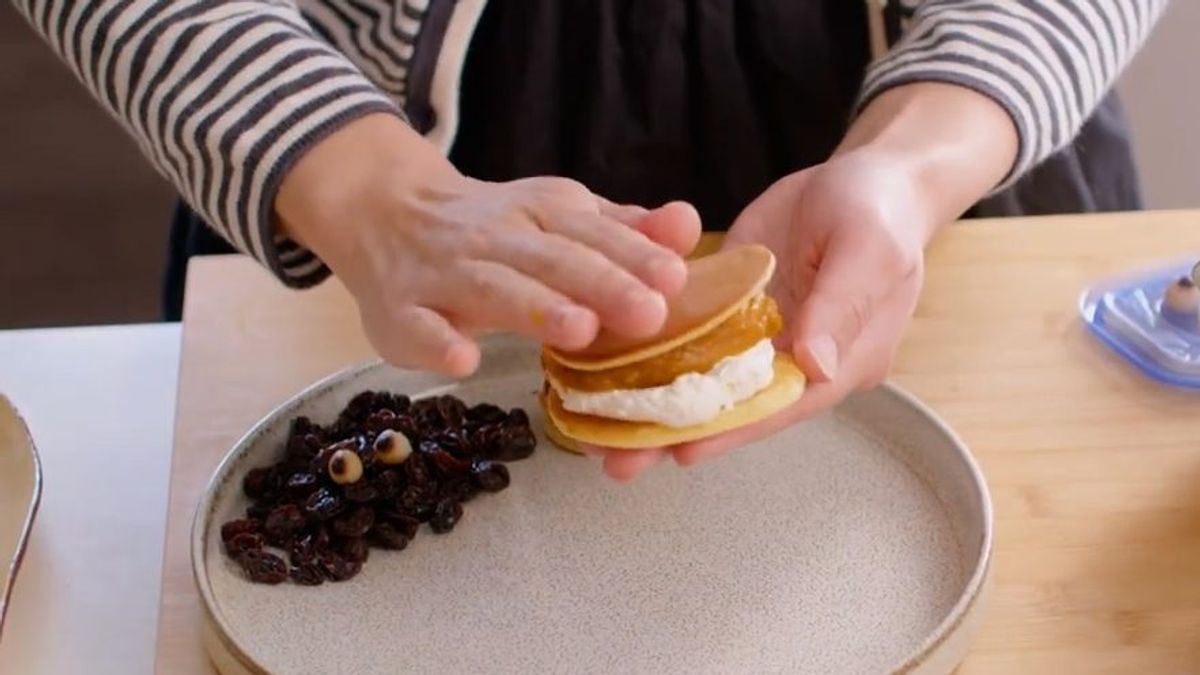 Person assembling dorayaki with red bean filling and white cream between two pancakes