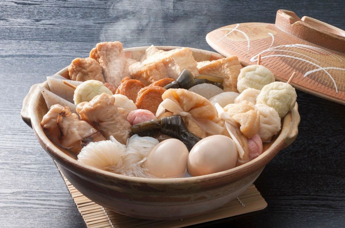Steaming hot pot with seafood, meat, vegetables, and eggs in clay bowl