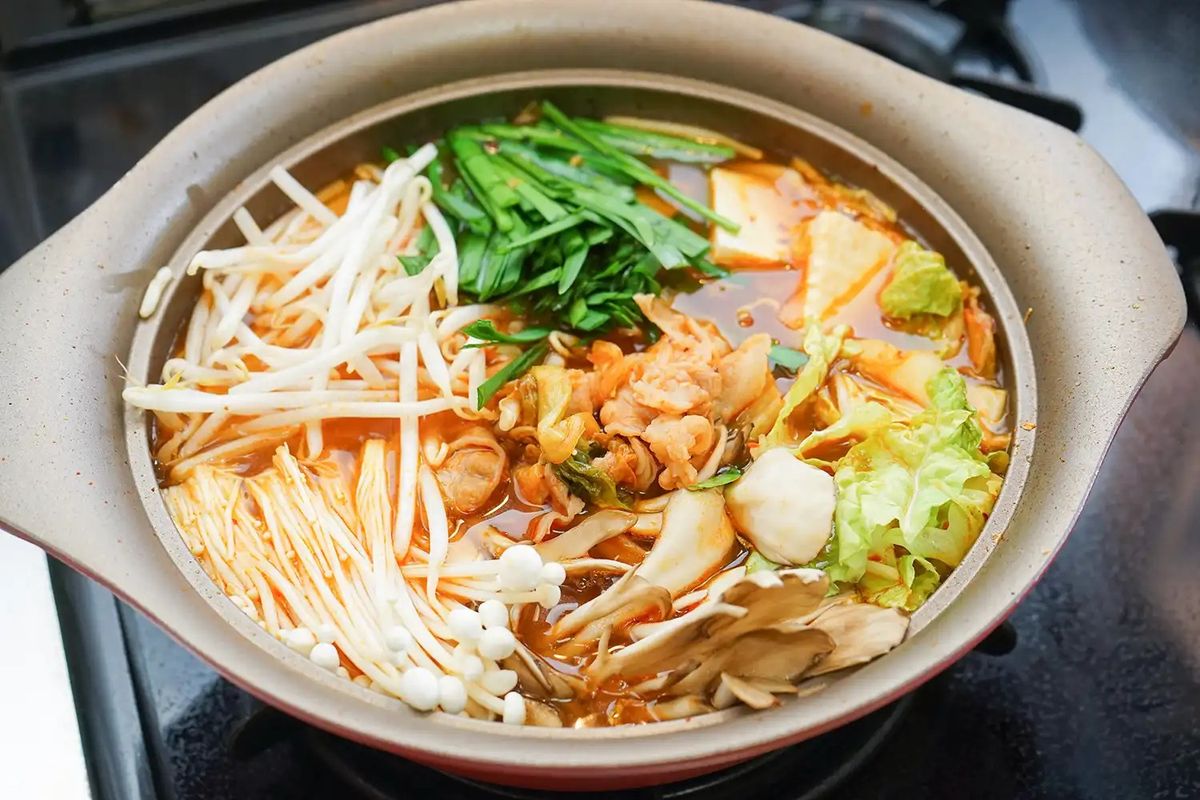 Hot pot with noodles, vegetables, mushrooms, and broth in ceramic bowl