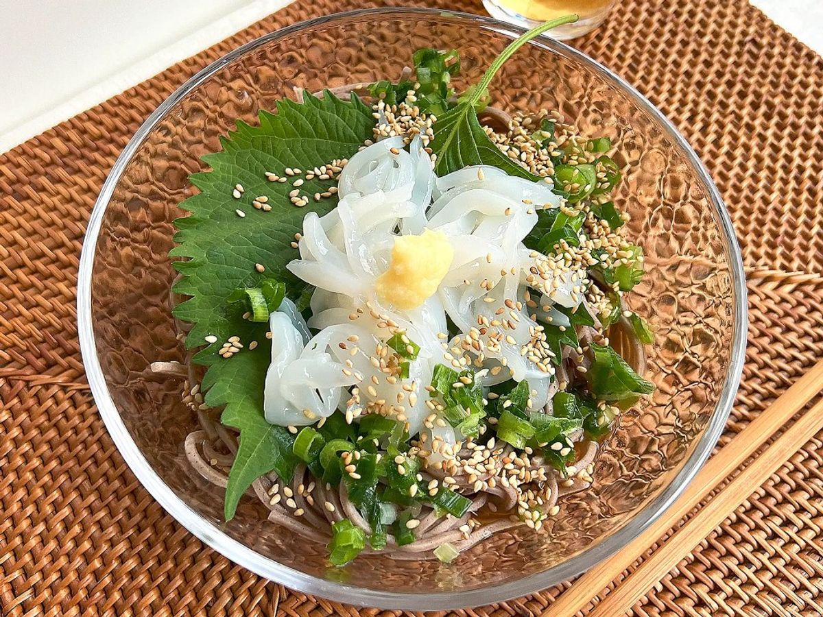 White flowers with sesame seeds and fresh greens in decorative glass bowl on woven placemat
