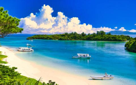 Tropical beach cove with turquoise waters, white sand, boats, and lush green islands