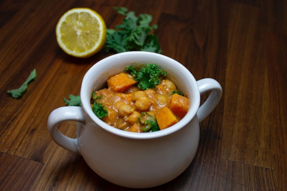 Chickpea curry with sweet potato and kale in white bowl, lemon garnish