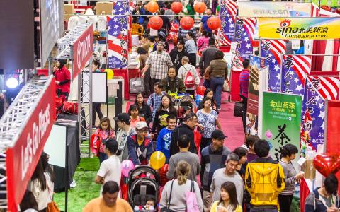 Crowded indoor Asian food festival with American and Chinese flags, vendor booths, families shopping