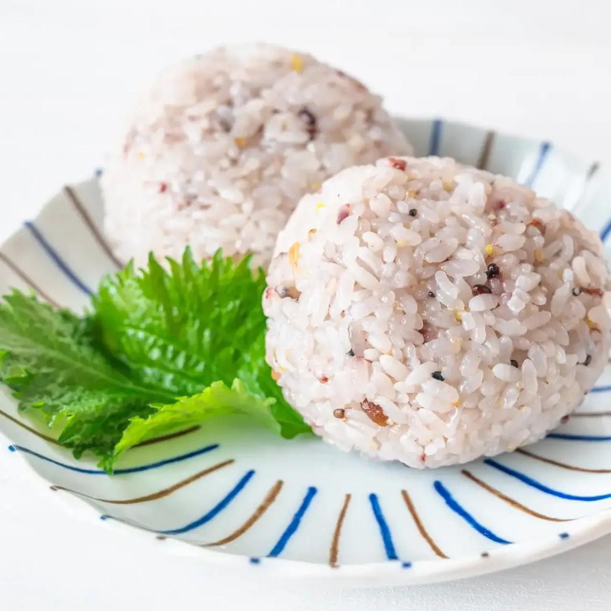 Two onigiri rice balls with mixed ingredients on decorative plate with shiso leaf