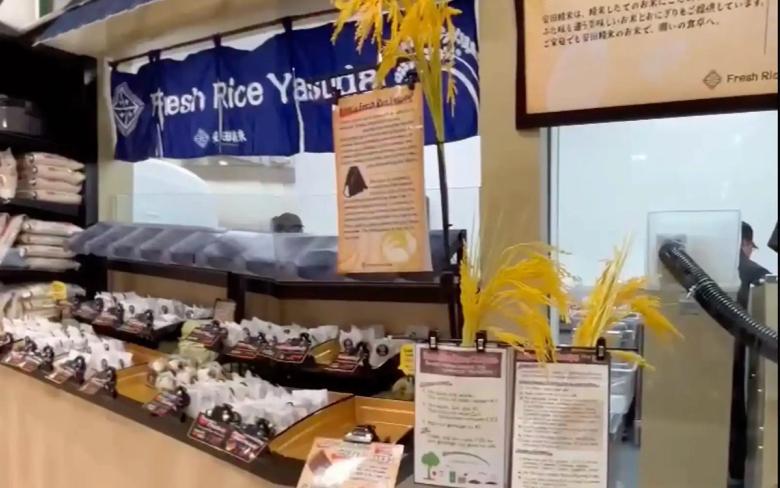 Fresh rice display stand with yellow decorative straw and product information cards in Japanese grocery store