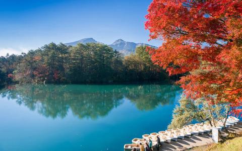 Autumn lake landscape with red maple trees, mountains, and clear blue water reflection