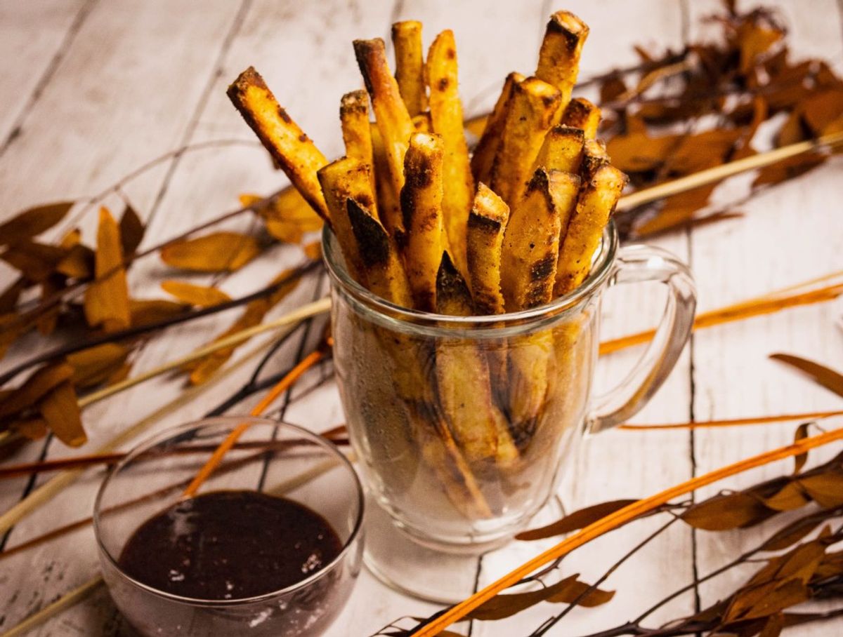 Golden crispy fries in glass mug with dipping sauce on wooden table