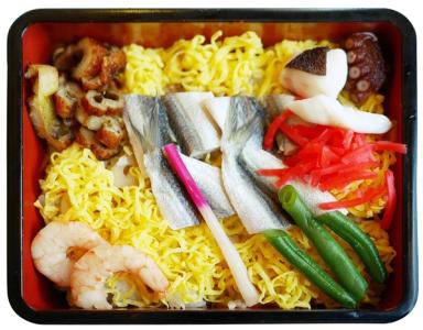 Japanese bento box with yellow noodles, fish, shrimp, vegetables, and pickled ginger
