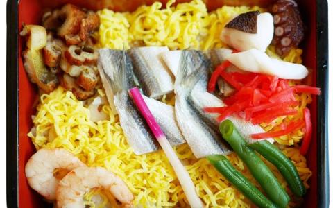 Japanese bento box with yellow noodles, fish, shrimp, vegetables, and pickled ginger