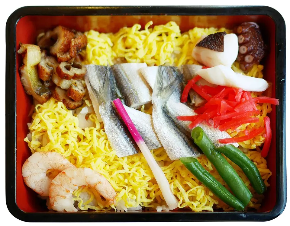Japanese bento box with yellow noodles, fish, shrimp, vegetables, and pickled ginger