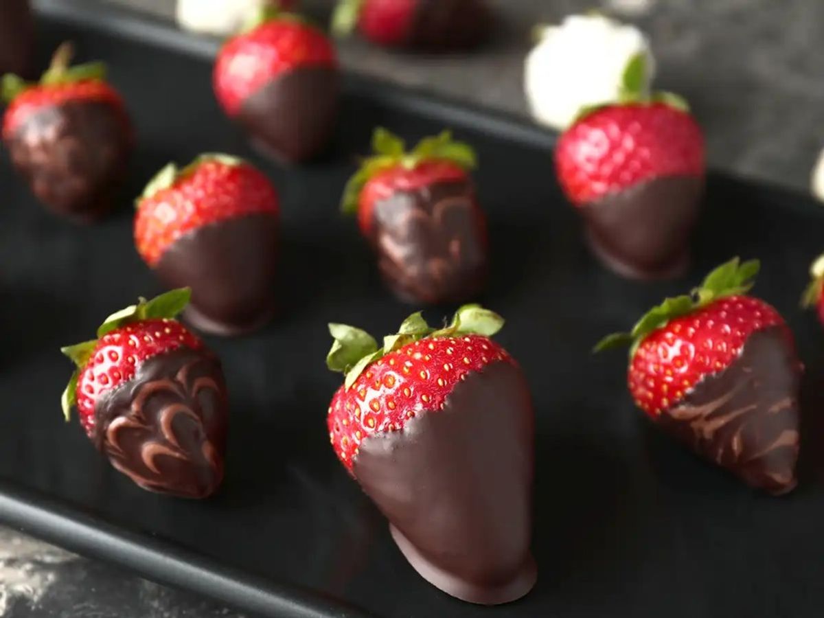 Chocolate-dipped strawberries with decorative cocoa patterns on black serving platter