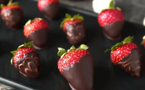 Chocolate-dipped strawberries with decorative cocoa drizzle on black plate