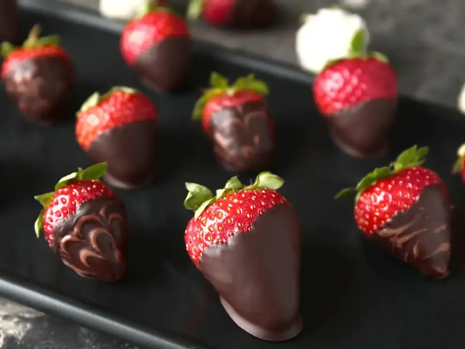 Chocolate-dipped strawberries with decorative cocoa drizzle on black plate