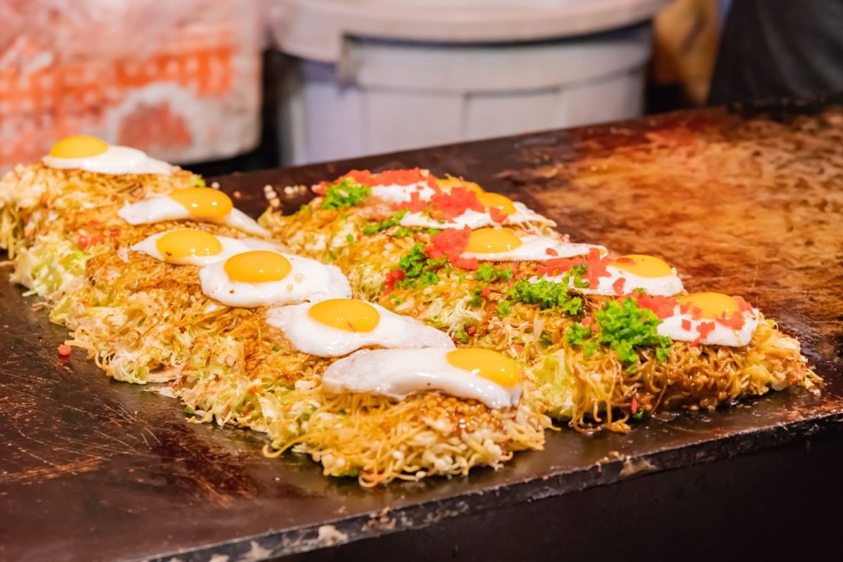 Okonomiyaki topped with mayonnaise, quail eggs, and pickled ginger on dark plate