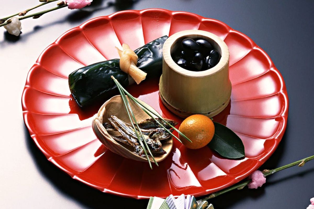 Red decorative plate with black olives, dried seaweed, small orange fruit, and condiment cup