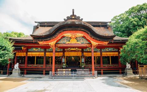 Traditional Japanese temple building with red pillars, curved black roof, and ornate decorations