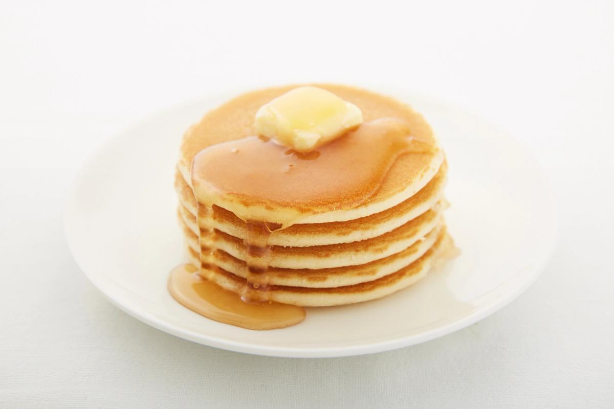 Stack of fluffy pancakes with butter and maple syrup on white plate