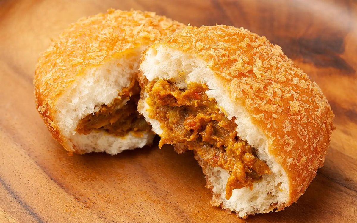 Vada pav cross-section on wooden surface showing crispy golden coating and spiced potato filling
