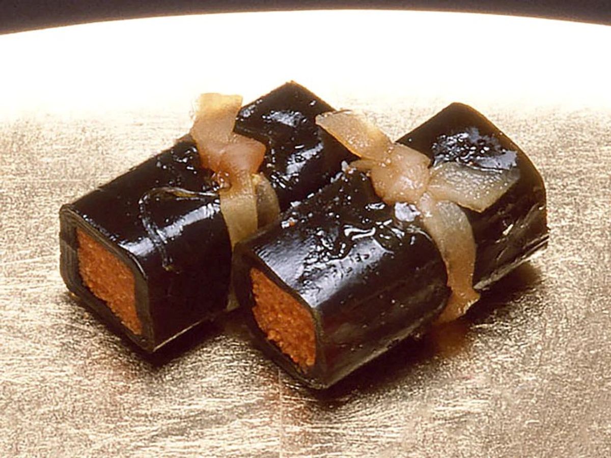 Two chocolate-glazed cakes with caramel garnish on gold surface
