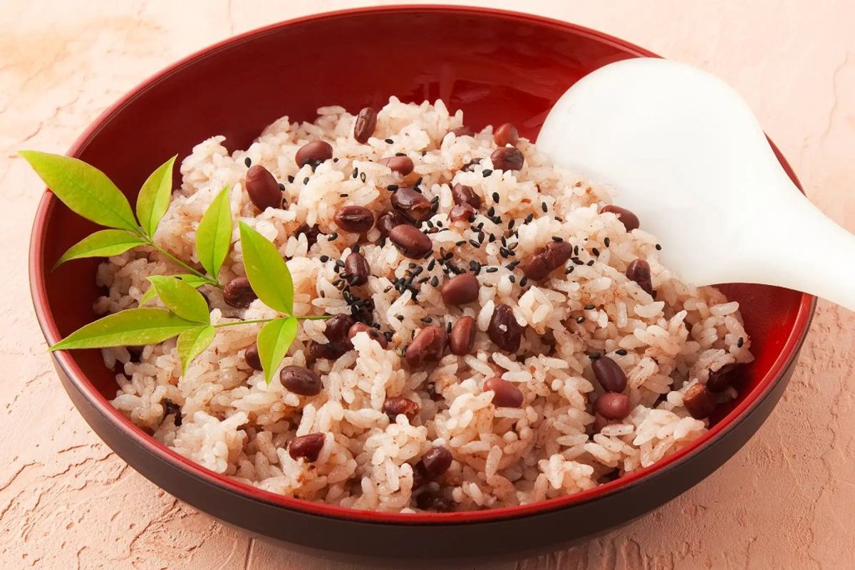 Red beans and brown rice in red bowl with white spoon and fresh garnish