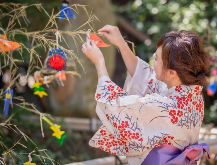 Woman in traditional áo dài decorating branch with colorful ornaments outdoors