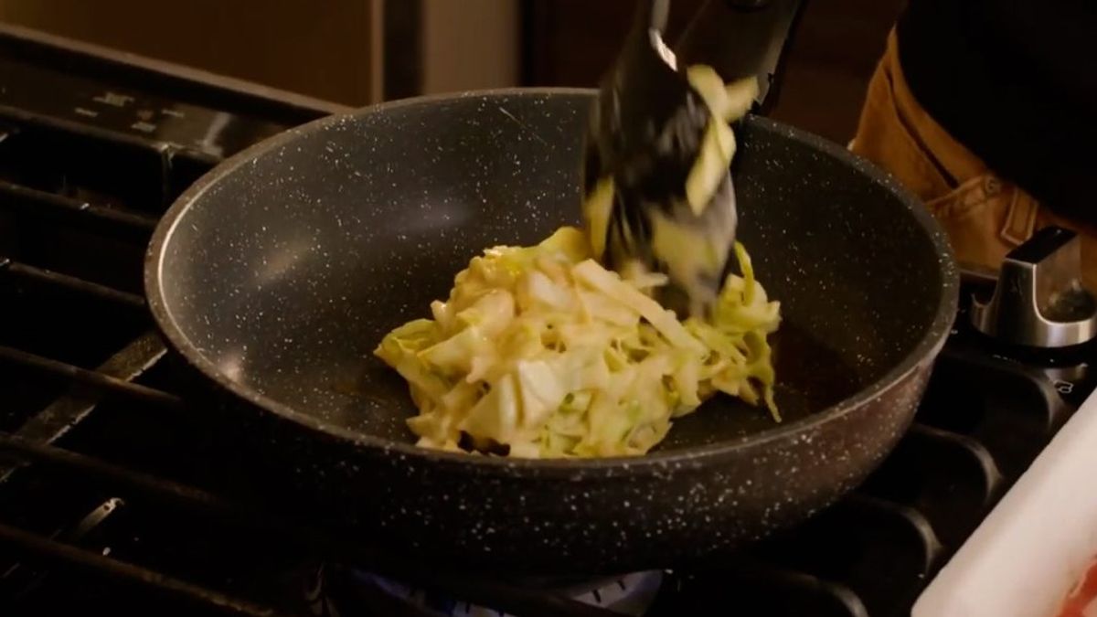 Grated daikon radish being added to a speckled wok on stovetop