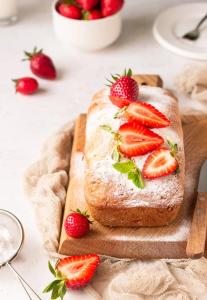 Strawberry loaf cake dusted with powdered sugar on wooden board with fresh berries