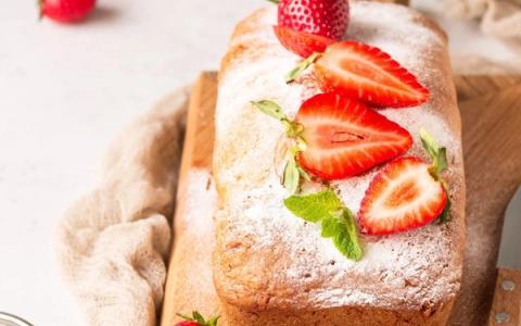 Strawberry loaf cake dusted with powdered sugar on wooden board with fresh berries