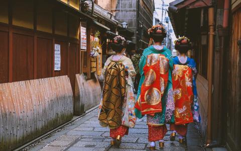 Three women in traditional kimono walking down historic Japanese alley with wooden buildings