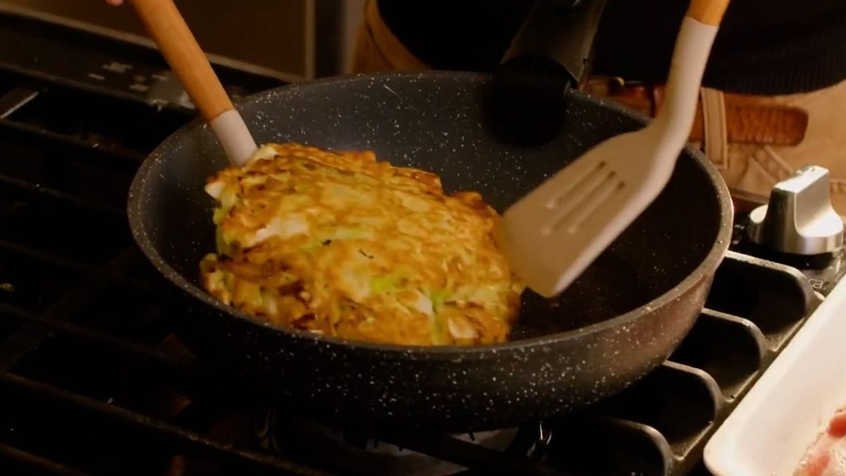 Cooking hash brown in speckled skillet on stovetop with spatula